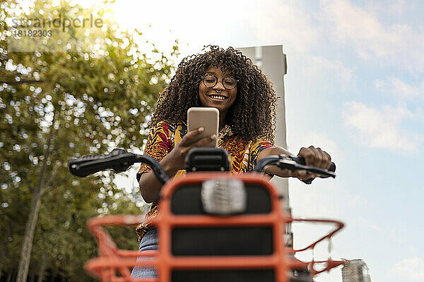 Lächelnde Frau auf dem Fahrrad mit Smartphone unter dem Himmel