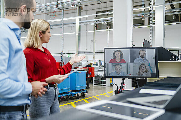 Geschäftsfrau gestikuliert mit Kollegin während eines Videoanrufs auf dem Computerbildschirm in der Fabrik