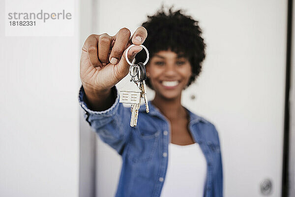 Glückliche Frau zeigt Hausschlüssel  die vor der Tür stehen
