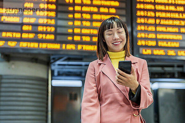 Glückliche junge Frau mit Mobiltelefon steht vor der Zeittafel