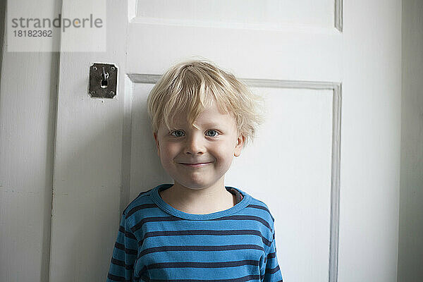 Porträt eines lächelnden kleinen Jungen vor einer weißen Tür