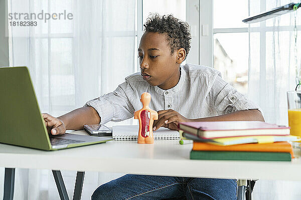 Junge macht Hausaufgaben mit Laptop und sitzt zu Hause am Tisch