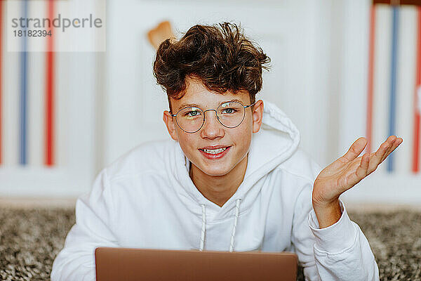 Lächelnder Junge mit Brille gestikuliert zu Hause