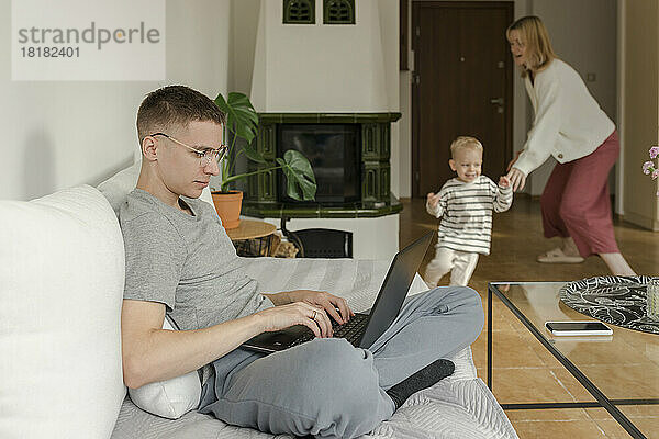 Junger Mann benutzt Laptop  Mutter und Sohn spielen im Hintergrund