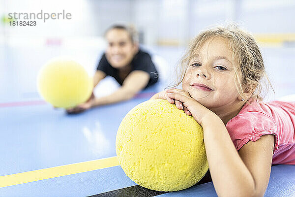 Mädchen ruht auf gelbem Ball und liegt auf dem Schulsportplatz