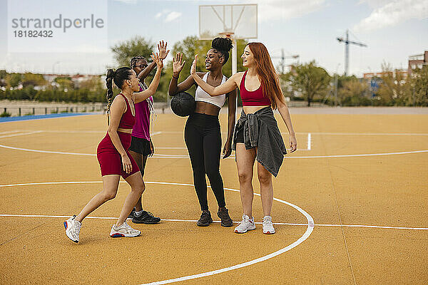 Fröhliche junge Freunde beim High-Five auf dem Basketballplatz
