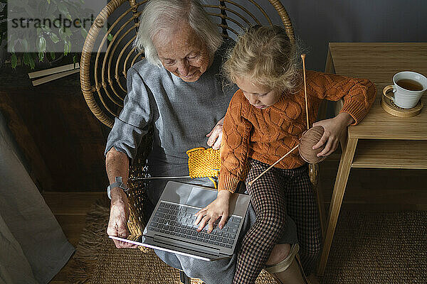 Großmutter und Enkelin lernen zu Hause das Stricken per Laptop