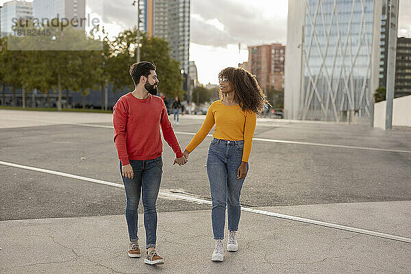 Junges Paar hält Händchen und geht am Fußweg entlang