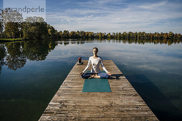 Frau praktiziert Meditation vor dem See an einem sonnigen Tag