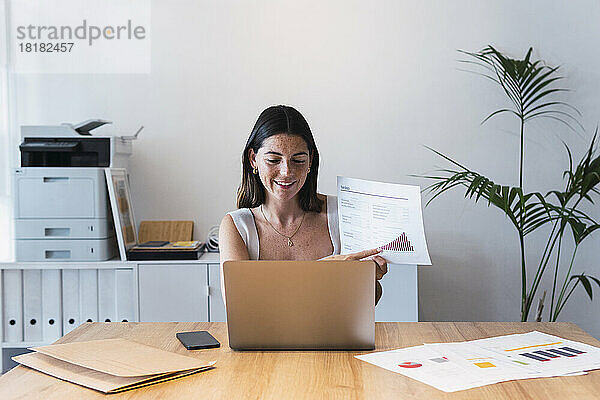 Junge Geschäftsfrau per Videoanruf über Laptop zeigt Diagramm im Büro