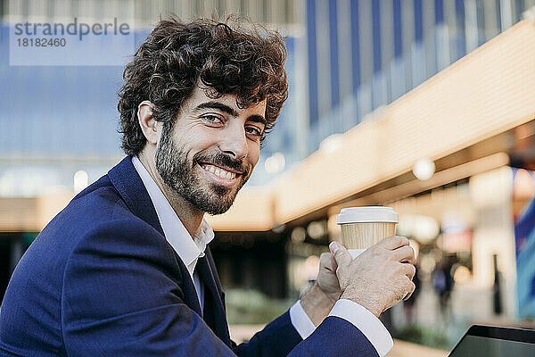Lächelnder junger Geschäftsmann mit Einwegkaffeetasse