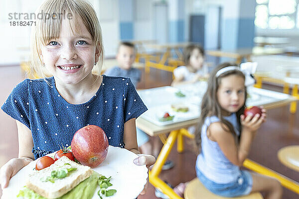 Girl holding plate with apple and sandwich at lunch break in school cafeteria