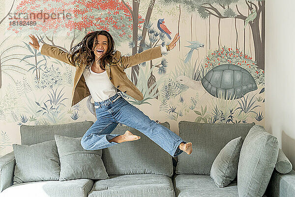 Fröhliche junge Frau springt zu Hause über Sofa im Wohnzimmer