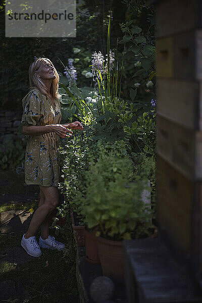 Reife Frau mit geschlossenen Augen steht neben Pflanzen im Garten