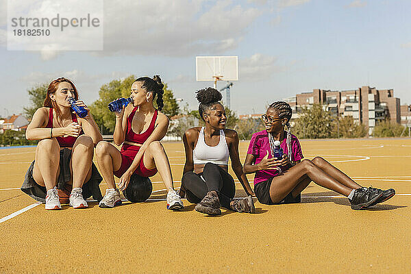 Junge Frauen trinken Wasser und sitzen mit Freunden auf dem Sportplatz