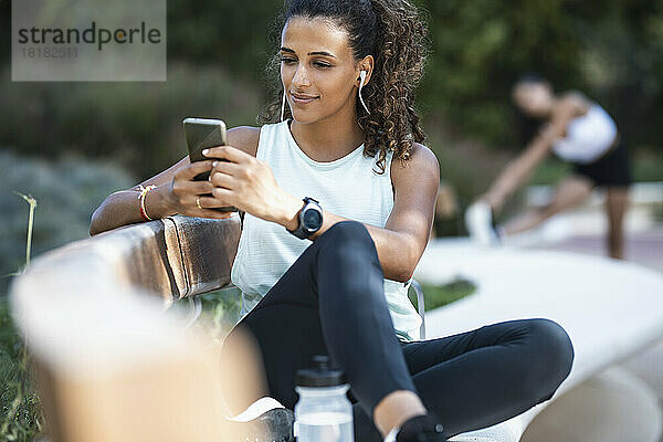 Lächelnde junge Frau benutzt Smartphone auf Bank