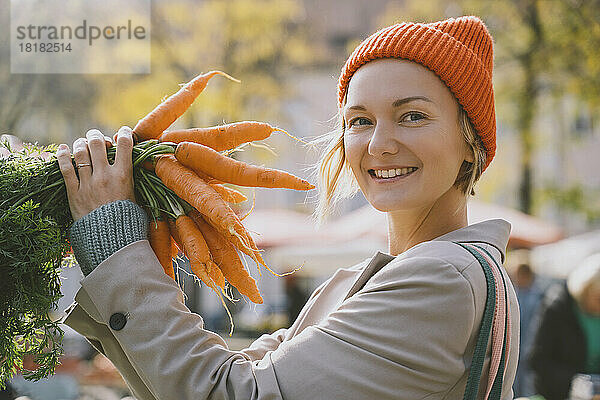 Glückliche Frau hält ein Bündel Karotten auf dem Markt
