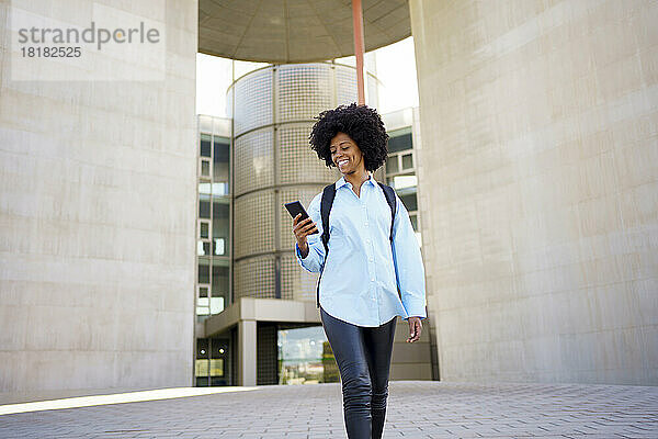 Glückliche junge Geschäftsfrau  die ihr Mobiltelefon vor dem Gebäude benutzt
