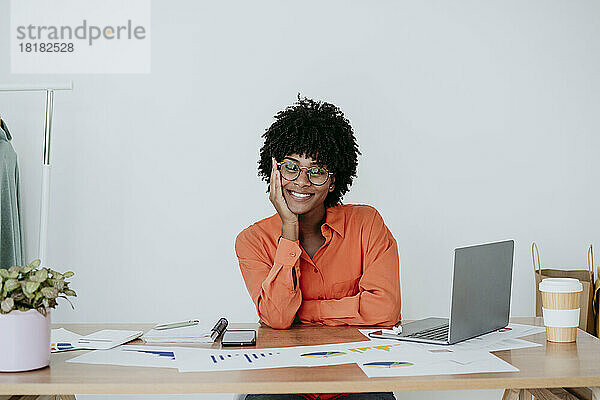 Glückliche Geschäftsfrau  die am Schreibtisch im Heimbüro sitzt und ihr Gesicht berührt