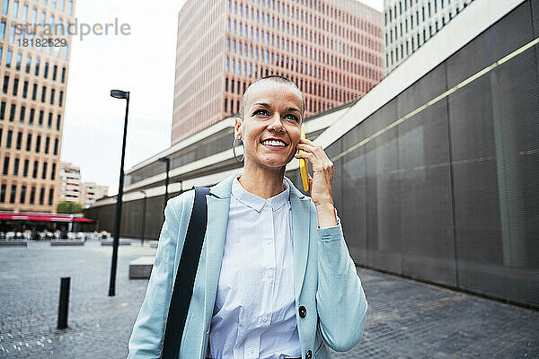 Glückliche Geschäftsfrau  die am Fußweg mit dem Smartphone spricht