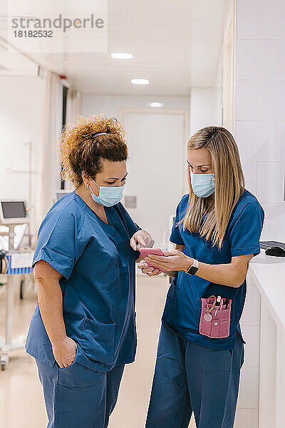 Ältere Krankenschwester diskutiert mit Kollegen über Smartphone im Krankenhaus