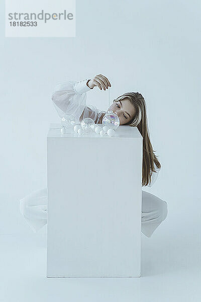 Girl playing with Christmas ball sitting behind table against white background