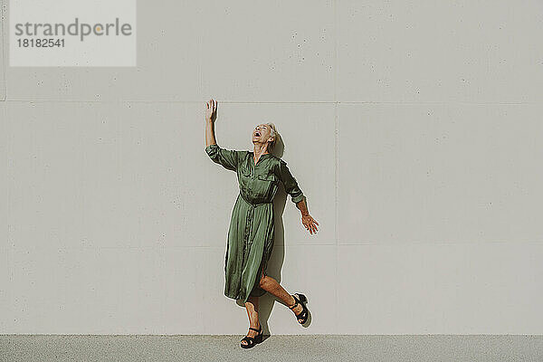 Reife Frau lacht an einem sonnigen Tag vor einer weißen Wand
