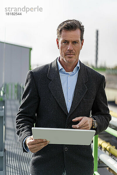 Reifer Geschäftsmann hält Tablet-PC in der Hand und steht in einer Industrieanlage