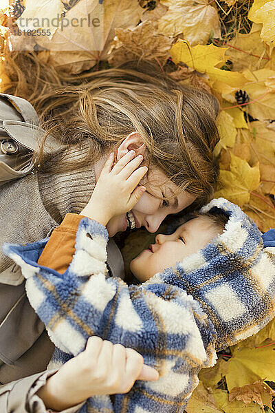 Mother and son lying on yellow autumn leaves in park