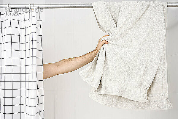Hand eines Mannes  der zu Hause ein Handtuch im Badezimmer hält