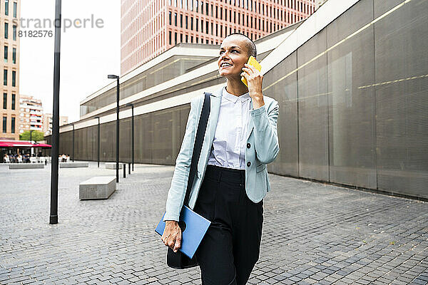 Lächelnde Geschäftsfrau  die am Fußweg mit dem Smartphone spricht
