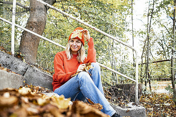 Reife Frau mit Herbstblatt sitzt am Geländer im Park