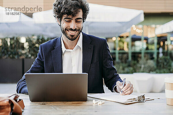 Lächelnder Geschäftsmann bereitet Strategie vor und schaut im Café auf Laptop