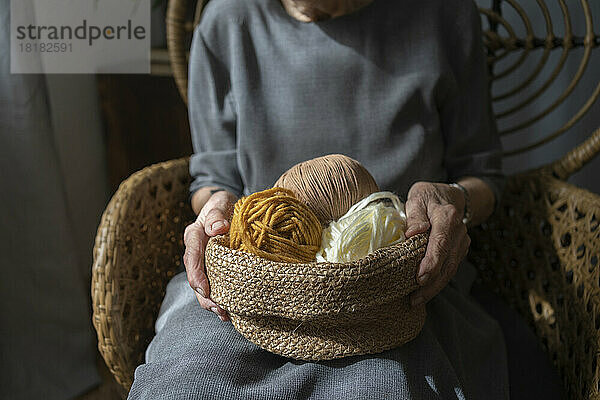 Hände einer älteren Frau  die zu Hause einen Korb mit bunter Strickwolle hält