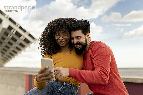 Glückliches junges Paar benutzt Smartphone unter bewölktem Himmel