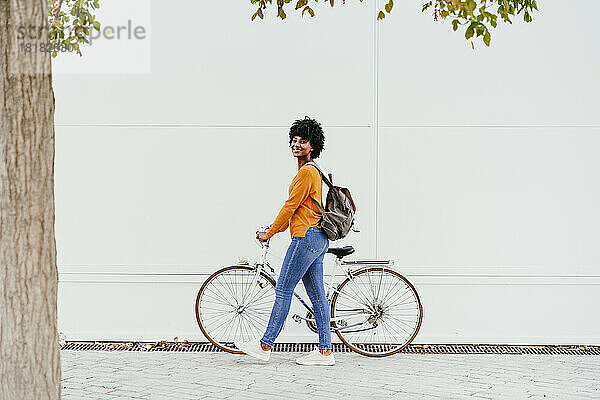 Lächelnde Frau mit Rucksack fährt Fahrrad auf Fußweg