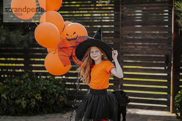 Mädchen mit Hexenhut und orangefarbenen Luftballons