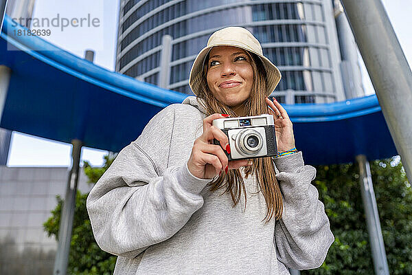 Lächelnde Frau hält Kamera vor Gebäude