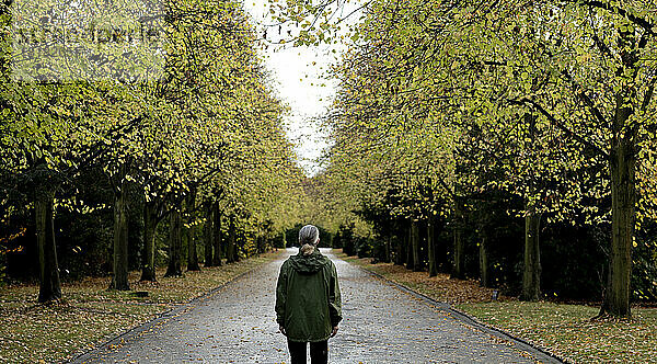 Ältere Frau steht auf einem Fußweg inmitten herbstlicher Bäume