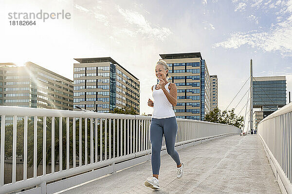 Reife Frau joggt auf Fußgängerbrücke in der Stadt