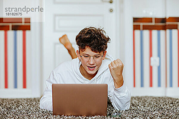 Happy boy gesturing fist looking at laptop