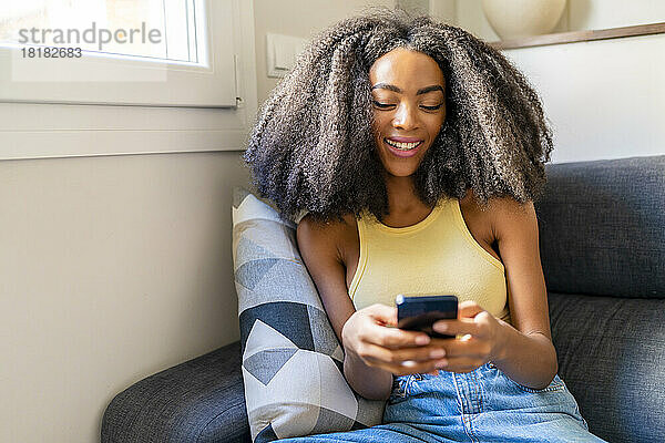 Frau mit Afro-Frisur nutzt Mobiltelefon zu Hause