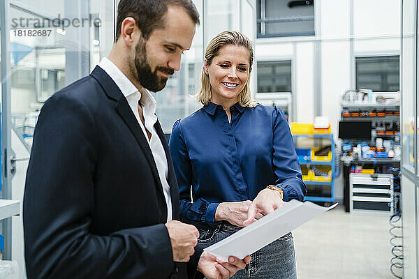 Lächelnde Geschäftsfrau diskutiert mit Geschäftsmann  der in der Fabrik ein Dokument hält
