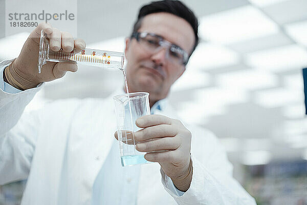 Chemiker gießt im Labor Lösung vom Reagenzglas in den Kolben