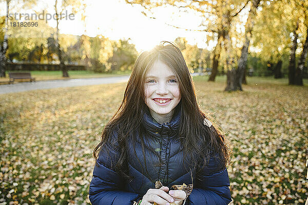 Lächelndes Mädchen in warmer Kleidung steht im Herbstpark