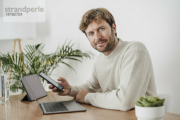 Geschäftsmann mit Mobiltelefon und Laptop am Schreibtisch im Büro