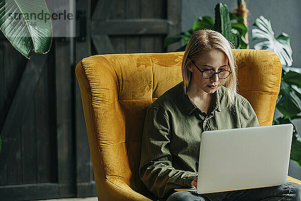 Geschäftsfrau sitzt mit Laptop im Sessel im Heimbüro