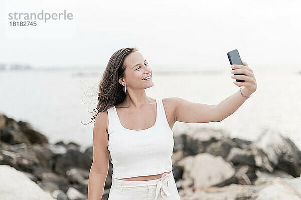 Lächelnde Frau macht im Strandurlaub ein Selfie per Smartphone