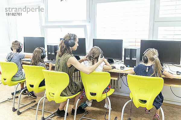 Lehrer und Schüler mit Kopfhörern sitzen auf einem Stuhl im Computerunterricht in der Schule