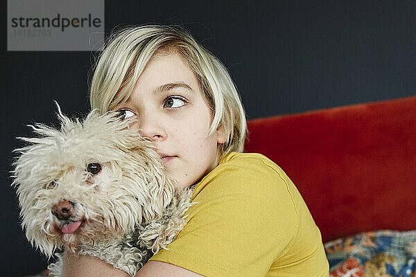 Junge mit blonden Haaren umarmt Hund zu Hause